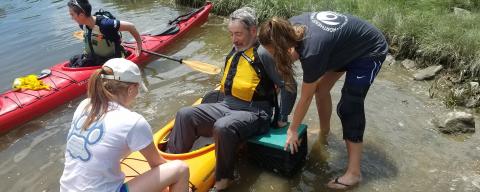 Interns assisting man into a kayak